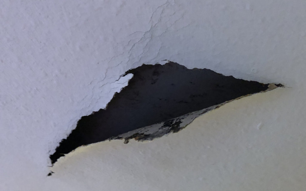Riss in der Decke und ein Stück weiße Tapete hängt herunter